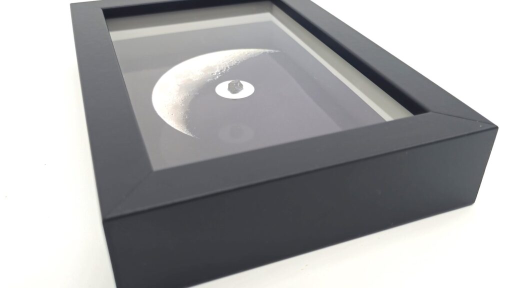Cadre noir en relief contenant une photographie de la Lune et un fragment de météorite