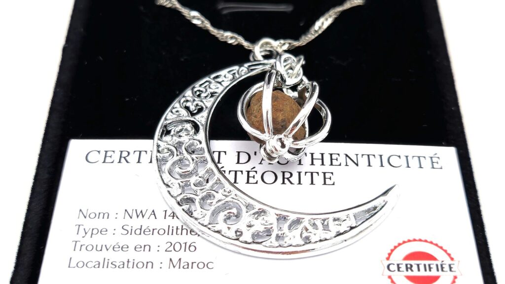 Pendentif croissant de lune en météorite posé sur son certificat d'authenticité, dans son écrin